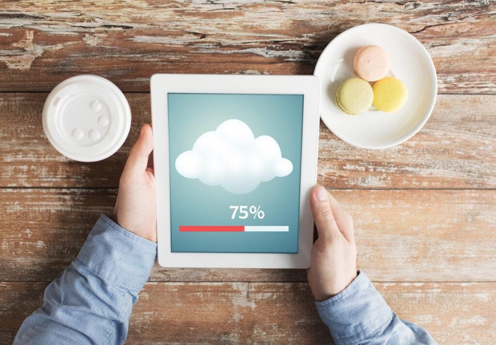 Mãosde um homem segurando tablet enquanto aguarda envio de documentos para a nuvem.