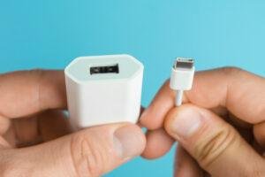 Carregador não funciona - Mãos de um homem sobre fundo azul, segurando um cabo e uma fonte de carregador