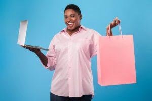 Mulher negra segurando um notebook e sacola de compras