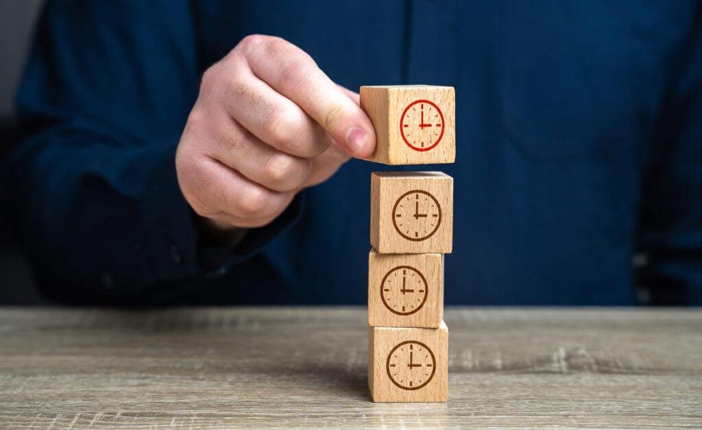 Foto das mãos de um homem empilhando pequenos blocos com desenho de um relógio em cada.