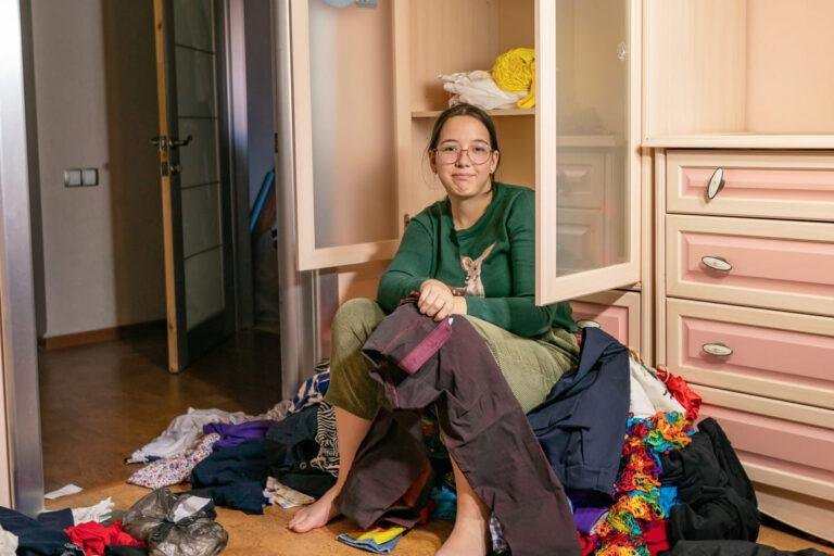 garota se senta em uma pilha de coisas jogadas fora do armário