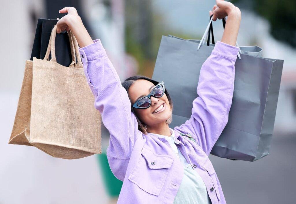 Imagem de uma mulher feliz, erguendo sacola de compras com os braços para o alto