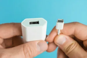 Carregador não funciona - Mãos de um homem sobre fundo azul, segurando um cabo e uma fonte de carregador